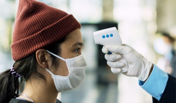 Woman in a medical mask getting her temperature measured by an electronic thermometer